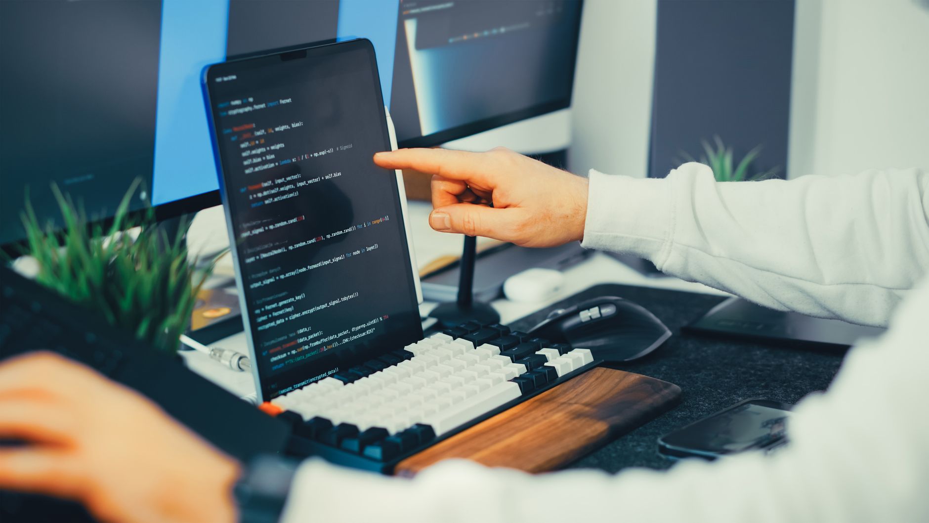 An engineer points at code on a screen while a colleague types, reviewing an AI-written script during human-in-the-loop incident response