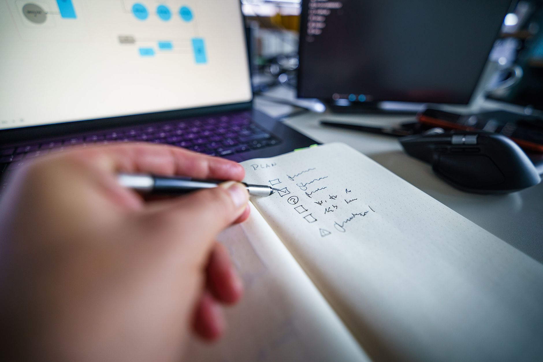Hand writing in notebook on a desk with laptop, showcasing productivity and organization skills, illustrating Datadog and SOC 2: Which Controls Datadog Covers and What Still Needs a Program