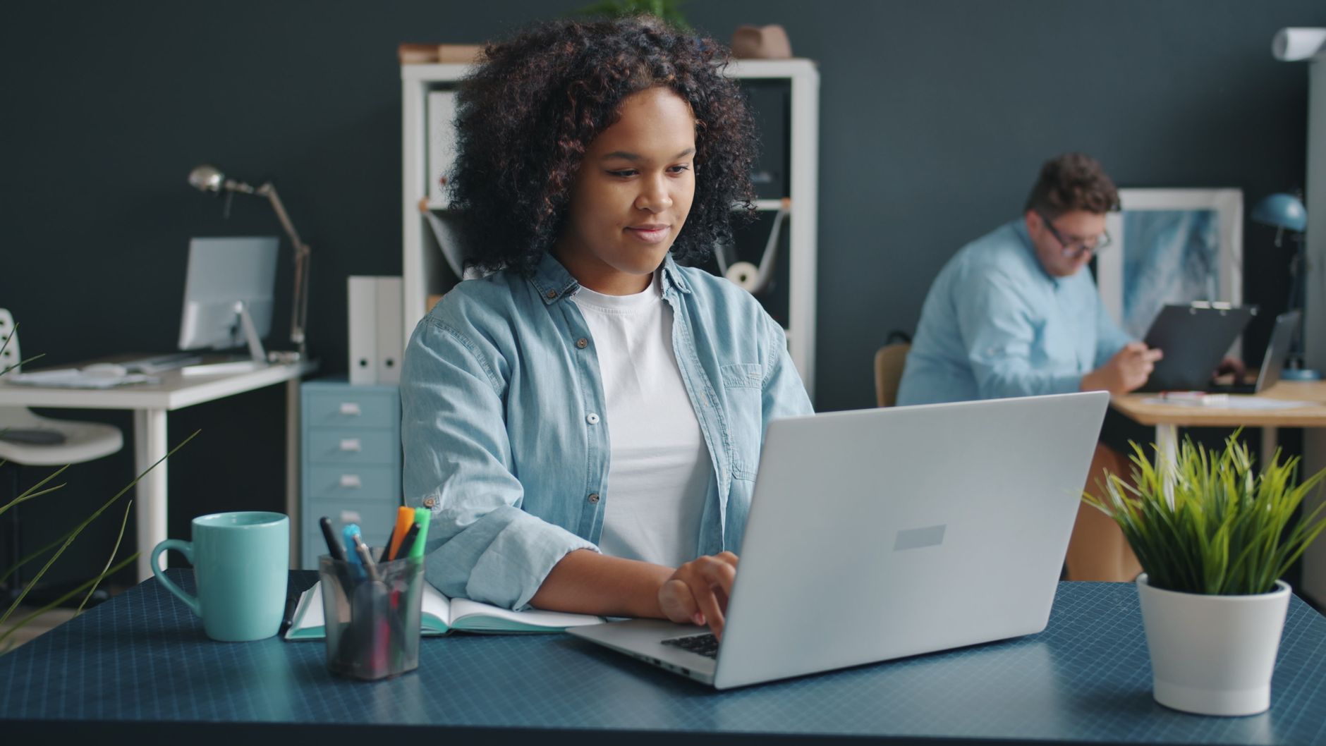 A young woman focused on her laptop in a contemporary office setting, promoting productivity, illustrating HR-Driven Provisioning in Microsoft Entra ID: Workday, SuccessFactors, Dayforce and Other HR Systems